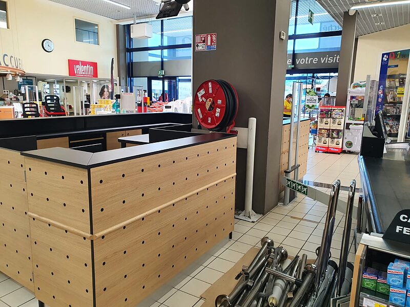 Banque d'accueil en chêne perforé et noir à l'entrée d'un Intermarché